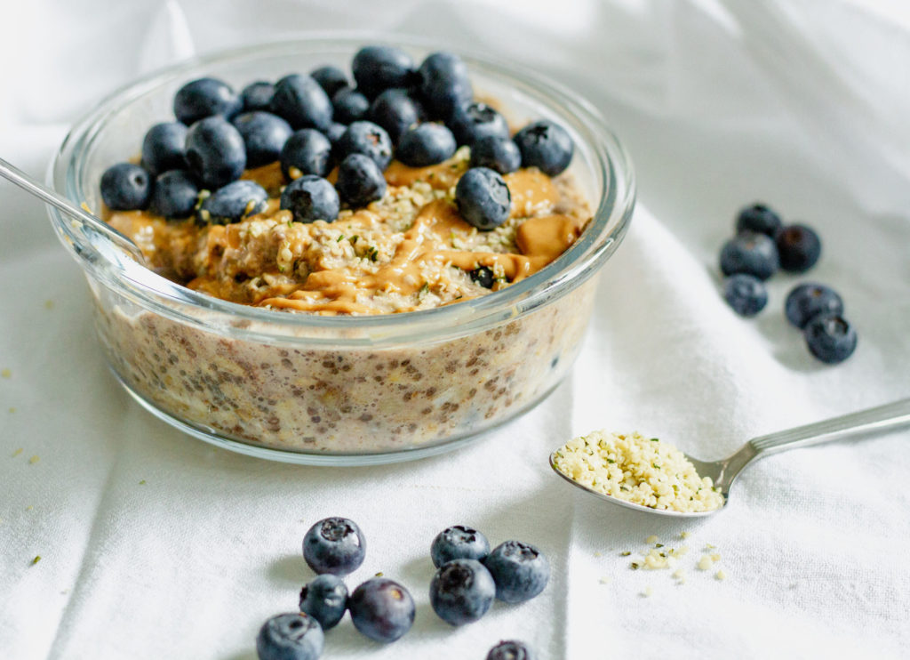 A bowl of oatmeal topped with blueberries and chia seeds on a table next to a spoon