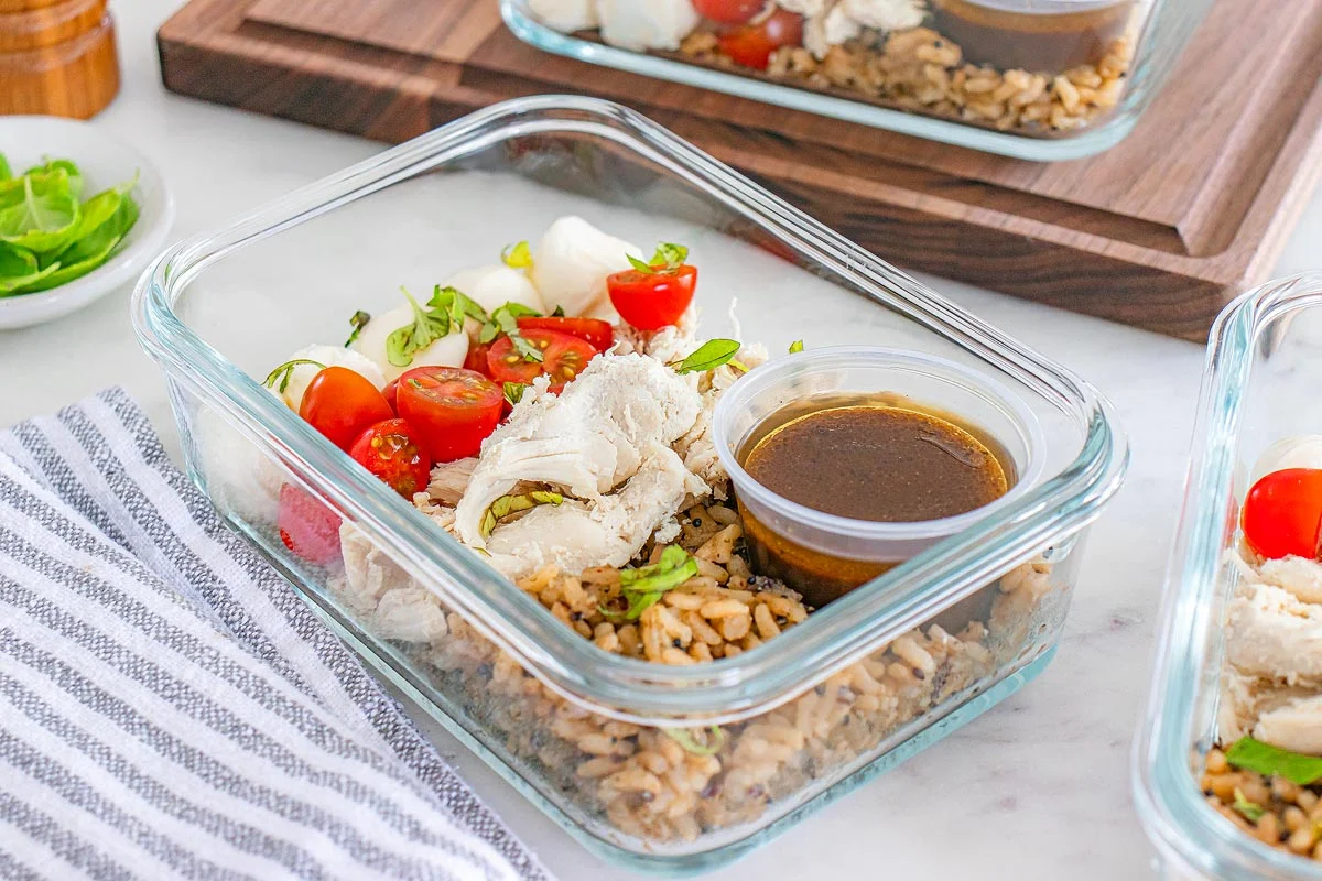 Glass meal prep containers on a kitchen counter filled with brown rice, roasted vegetables, and a small container of chickpeas